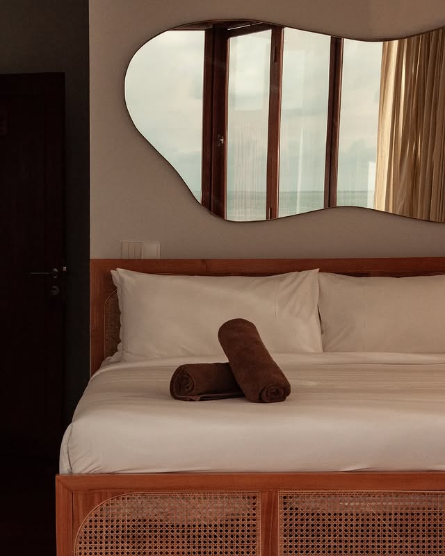 Ohm room bed beneath an organic-shaped mirror facing the ocean